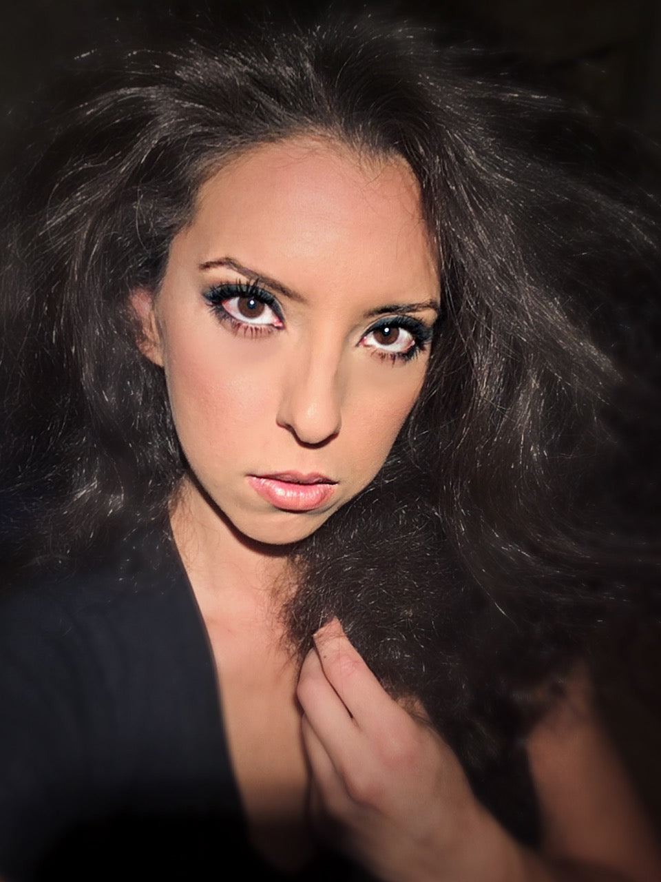 Woman with dark hair and dramatic makeup against a dark background