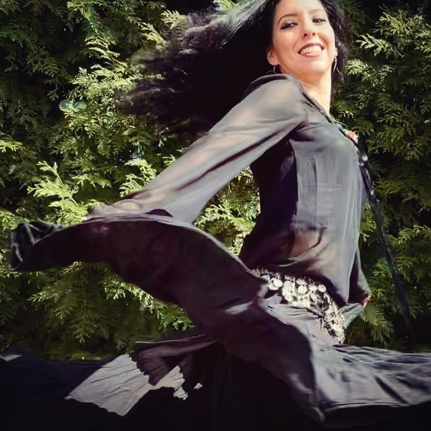 Woman Rachel Ingrid in a magical flowing black dress with a blurred background of greenery and nature